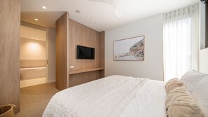 A bedroom with a large bed, a mounted TV, a framed picture on the wall, and a bathroom visible through an open door. - Oceano Residence Mornington (Mornington)