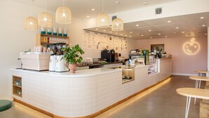 Een modern café met een witte betegelde toonbank, koffieapparaten en hangende pendelverlichting.
