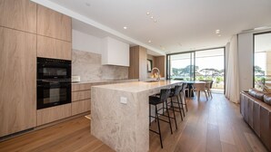 Een moderne keuken met houten kastjes, een marmeren eiland en een zithoek met barstoelen.