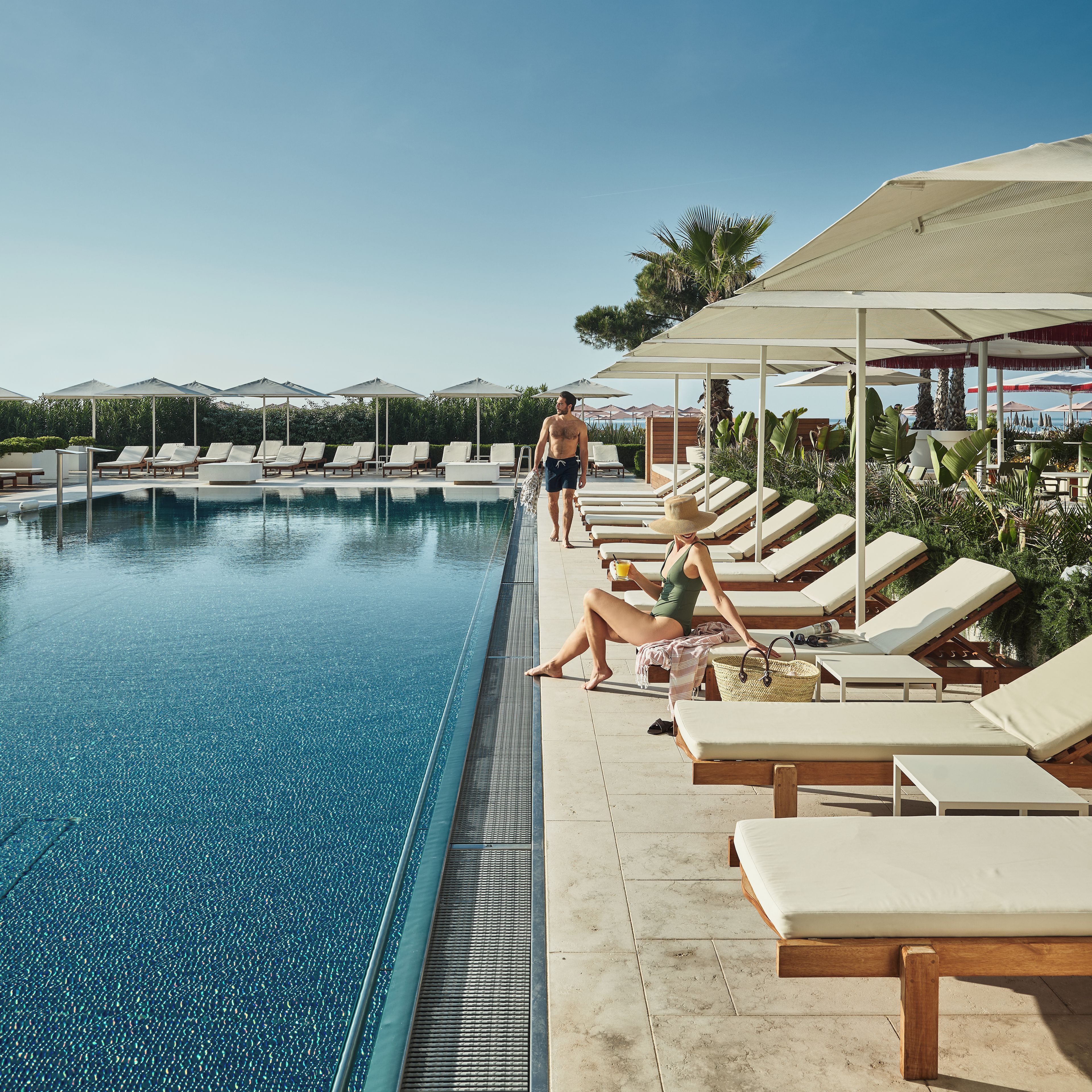 A pool area with lounge chairs and umbrellas, a clear sky, and a person walking by.