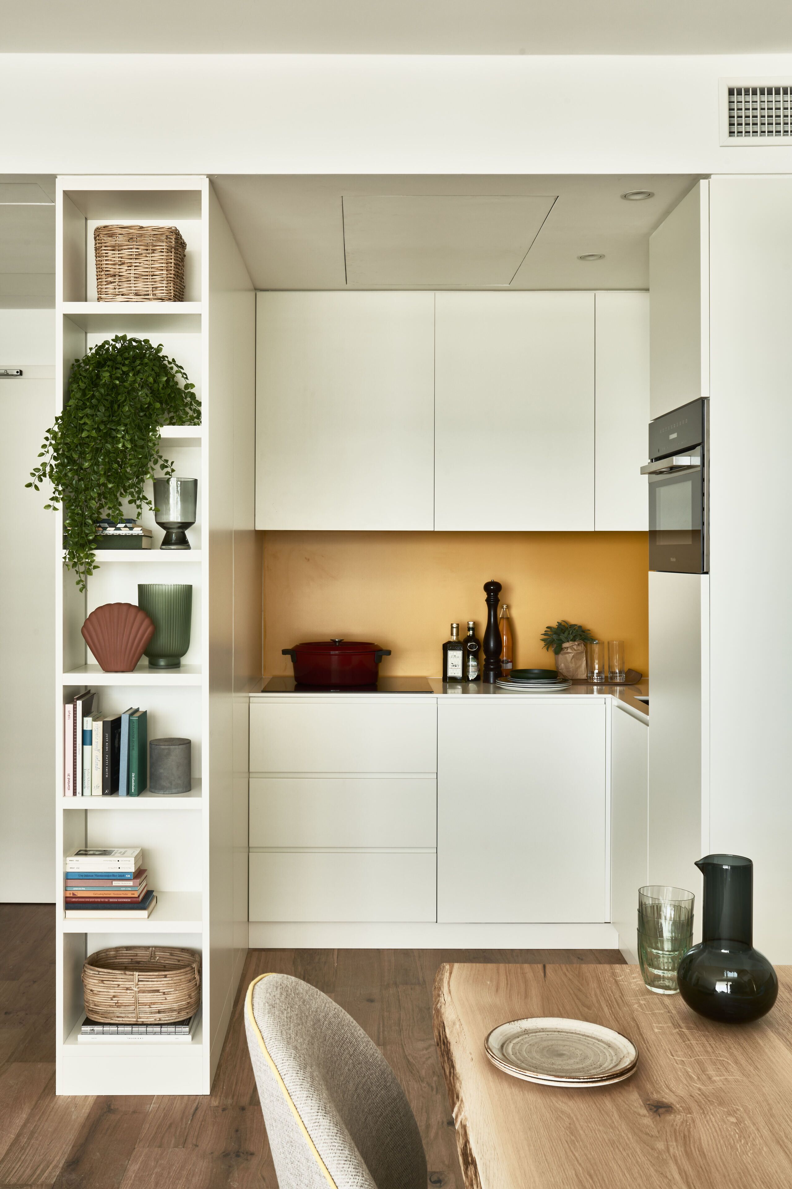 Una cocina moderna con armarios blancos, una mesa de comedor de madera y una estantería empotrada.