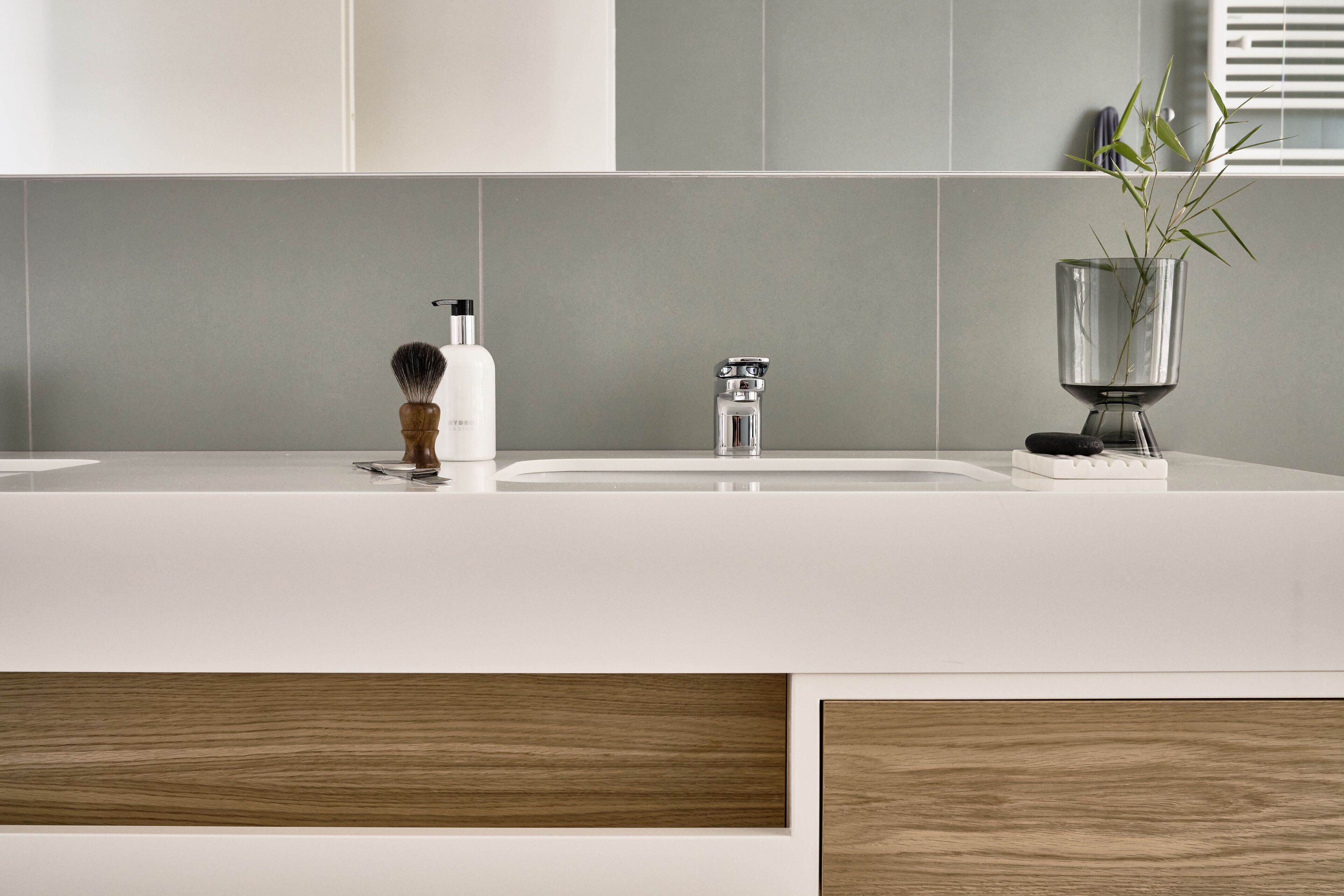 A modern bathroom with a white sink, a wooden shaving brush, and a glass vase with a plant.