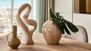 Une chambre moderne avec vue sur la plage, une table en bois agrémentée d’objets décoratifs et une grande fenêtre avec des rideaux.