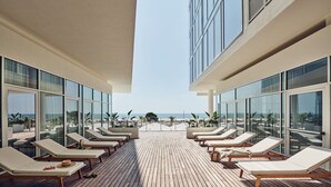 Une terrasse ensoleillée avec des chaises longues et vue sur la plage.