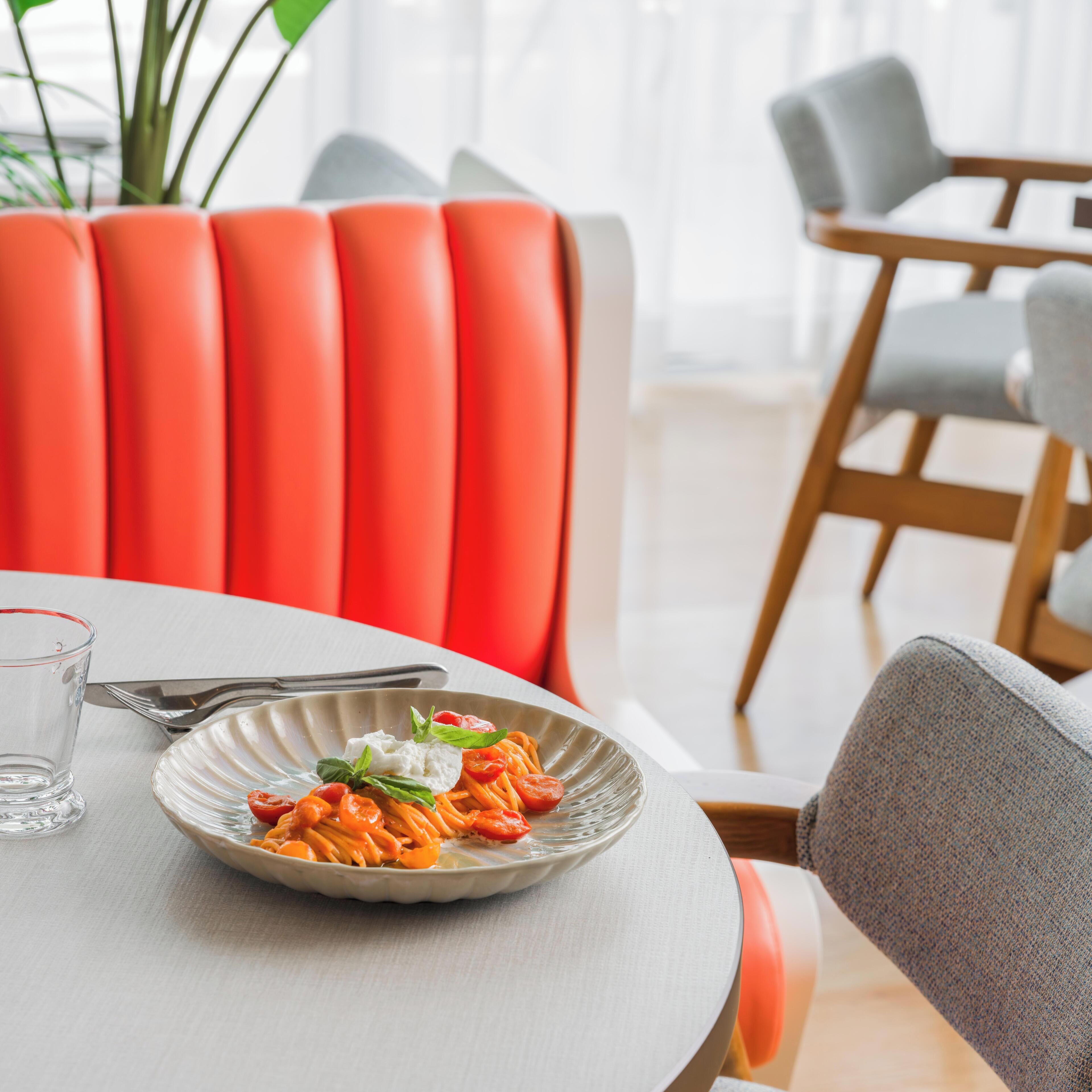 Une table à manger avec une assiette de pâtes, un verre d’eau et des couverts.