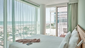 Une chambre d’hôtel avec un grand lit, une vue sur la plage et la ville, et un balcon donnant sur la plage.