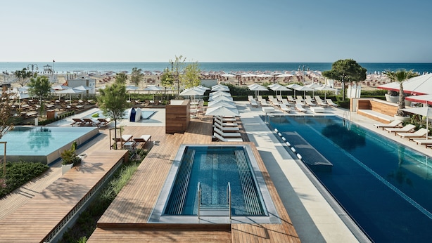 Un espace piscine aménagé dans un complexe hôtelier, comprenant une grande piscine, des chaises longues et des parasols.