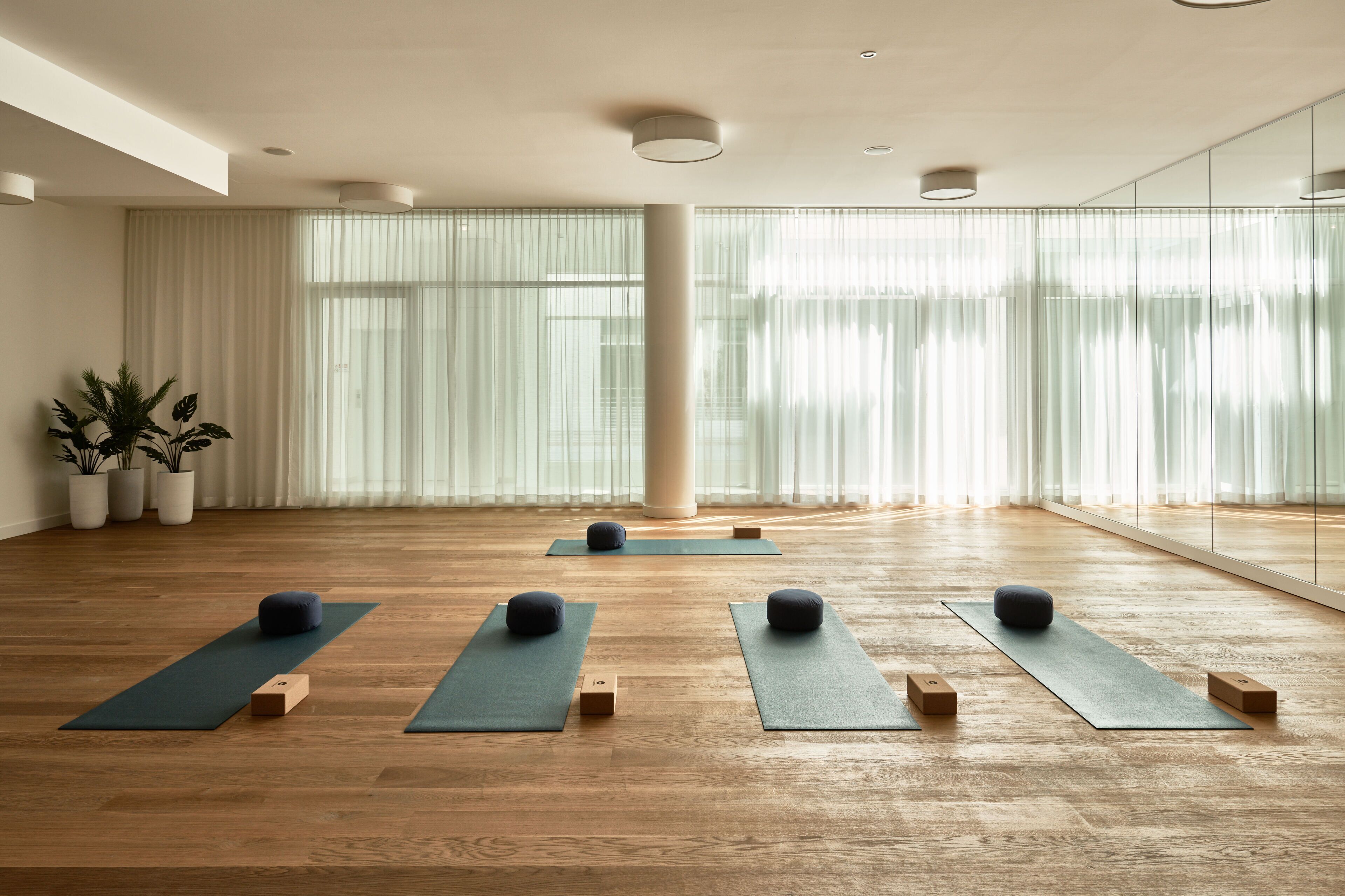A spacious room with wooden flooring, large windows with sheer curtains, and yoga mats arranged for practice.