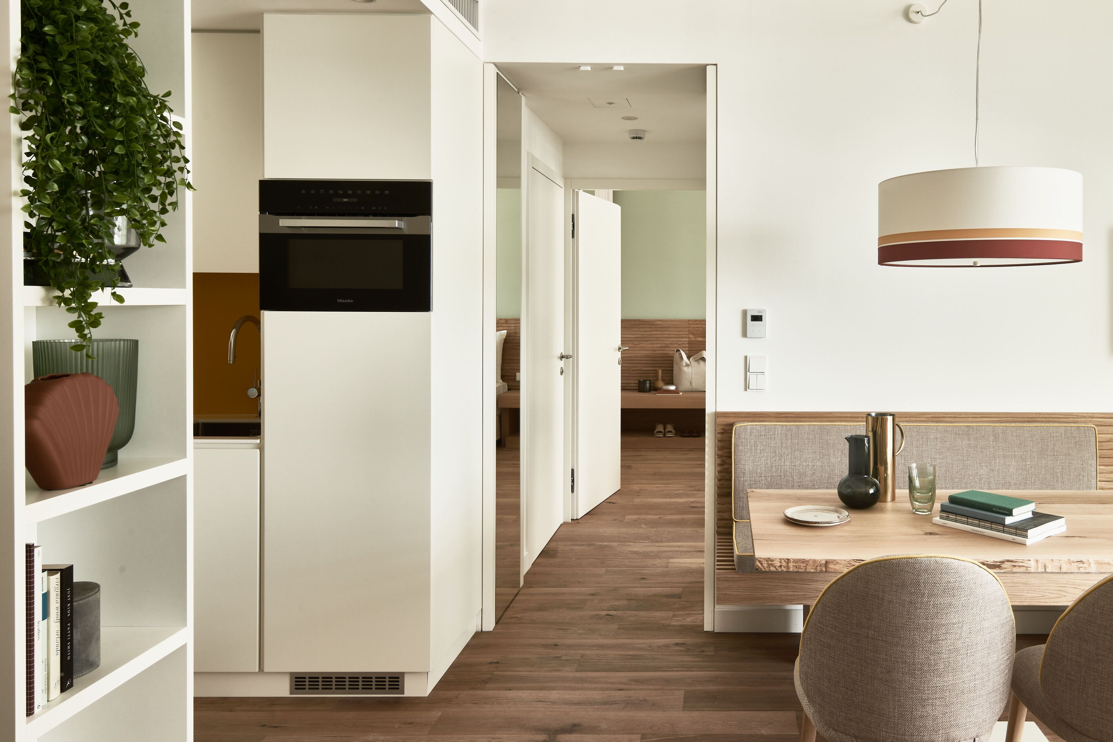 Una cucina moderna con mobili bianchi, forno integrato e zona pranzo con tavolo e sedie in legno.