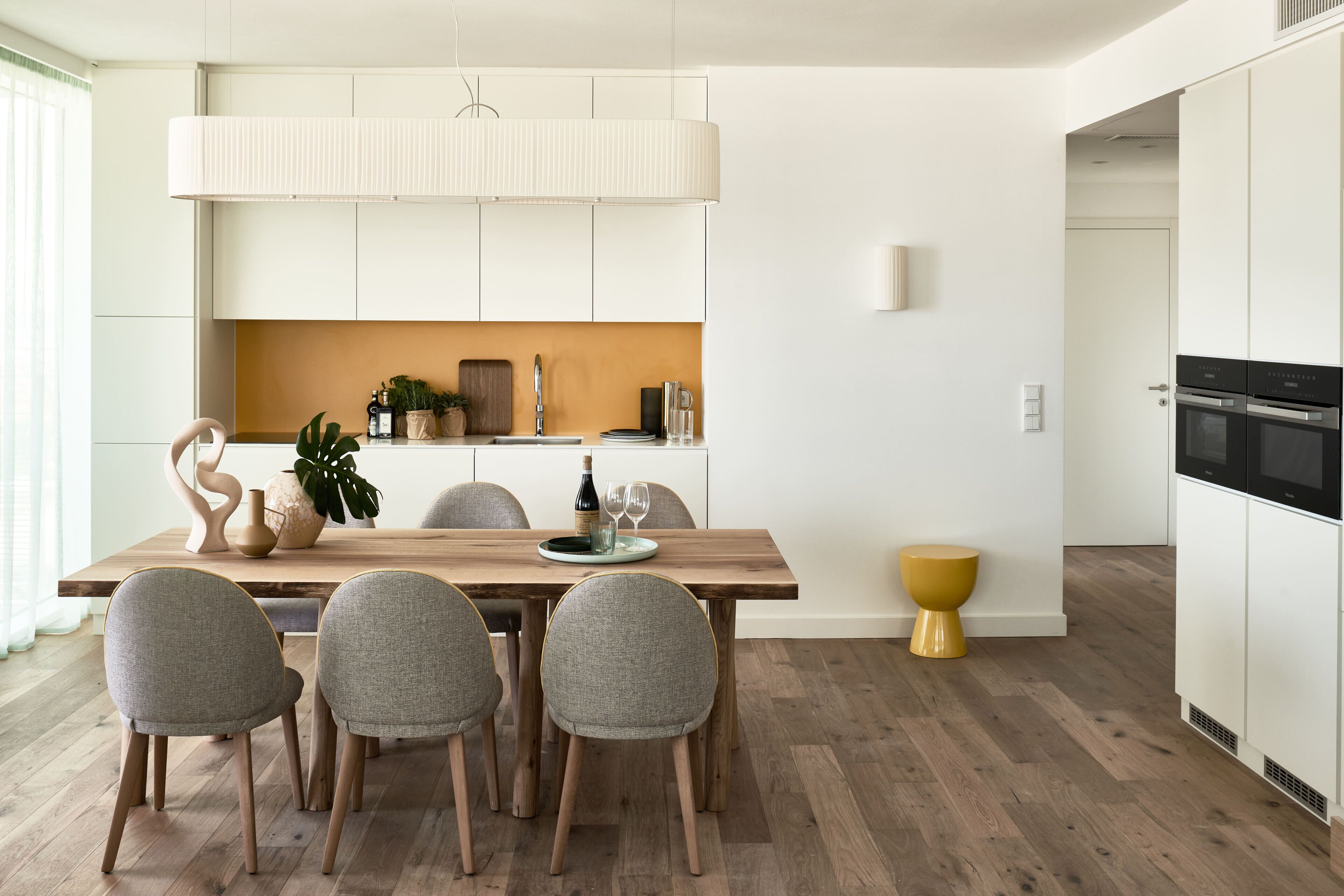 Une cuisine moderne avec des meubles blancs, une table à manger en bois et des chaises grises.