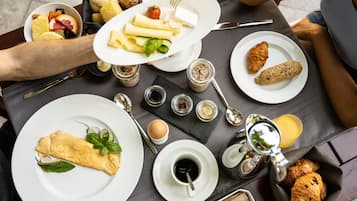 Une table dressée avec des aliments pour le petit-déjeuner, notamment des œufs, des croissants et une omelette roulée, ainsi que des condiments et une machine à café.