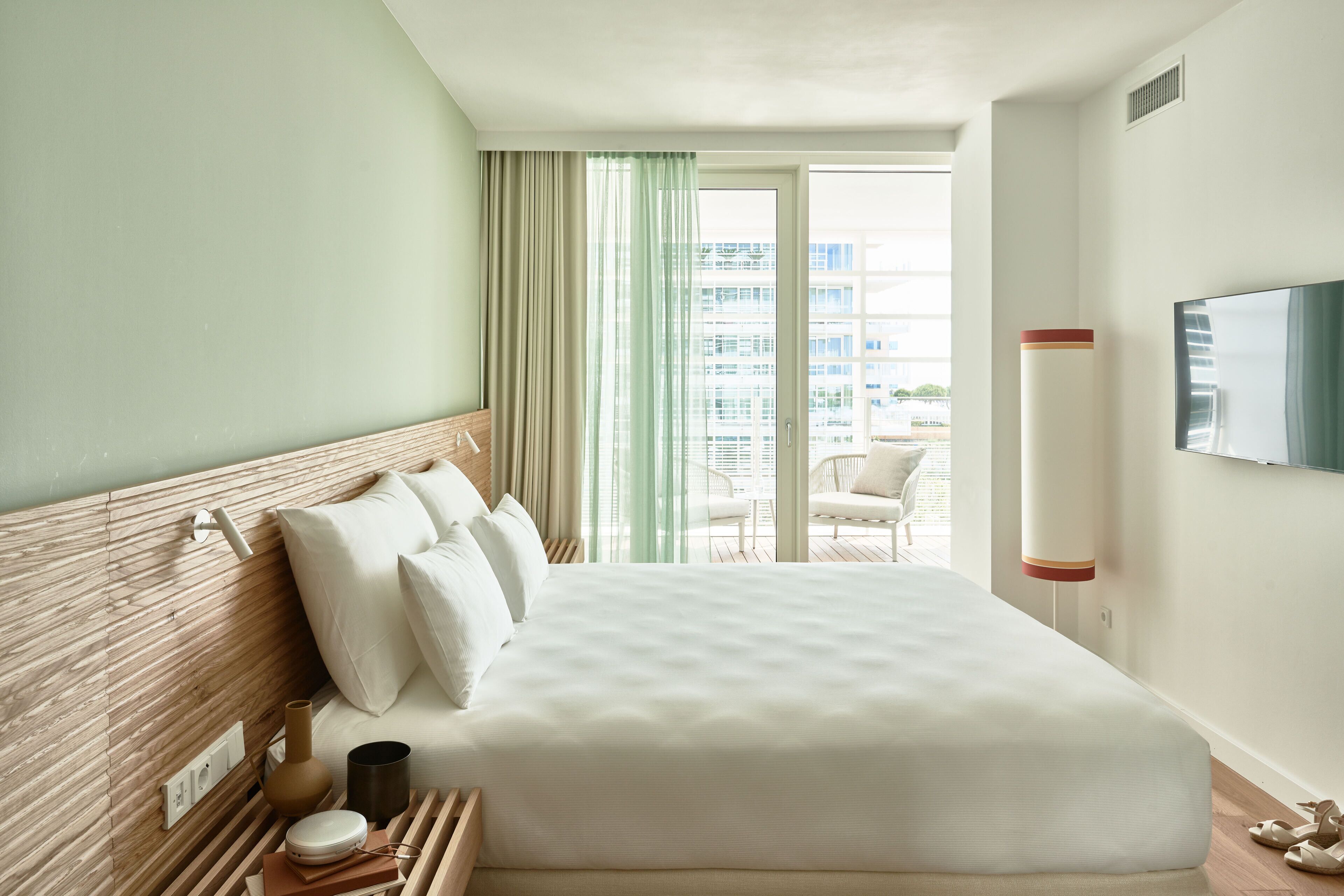 Een hotelkamer met een groot bed, een houten hoofdbord, een flatscreen televisie aan de muur en een balkon met uitzicht op de stad.