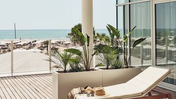 Un balcon avec vue sur la plage, des chaises longues et des plantes en pot.