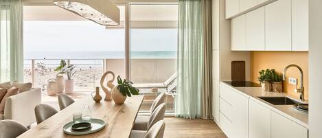 A modern kitchen with a view of the sea, a dining area with a wooden table, and a balcony with a view.