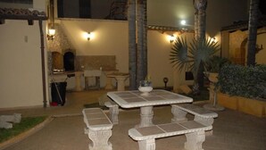 An outdoor patio with stone tables and benches, surrounded by palm trees and a stone wall. - PRESTIGIOSA E SINGOLARE VILLA CON APPARTAMENTO CAMERE E PISCINA AD USO ESCLUSIVO (MAZARA DEL VALLO)