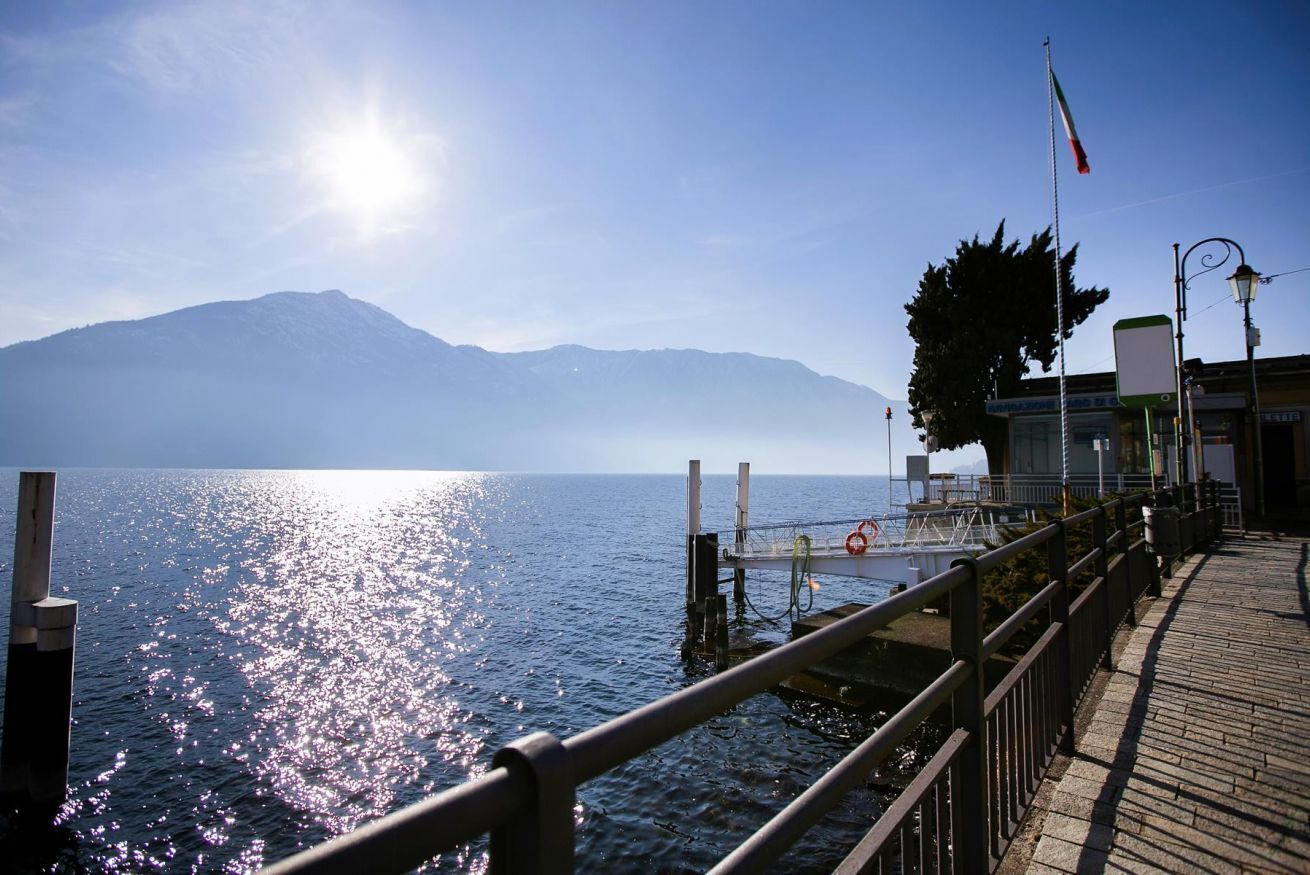 A waterfront view with a dock, a mountain in the background, and a flag on a pole.