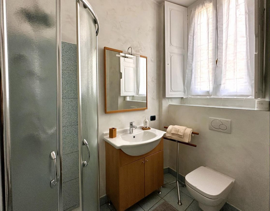 A bathroom with a glass shower enclosure, a wooden vanity with a sink, a mirror, and a toilet.