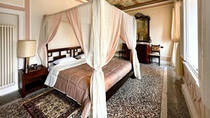 A four-poster canopy bed with a wooden headboard, a nightstand with a lamp, a mirror, and a carpeted floor. - Cà del Conte Lake Como (Tremezzo)