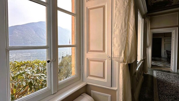 A room with a large window offering a view of a lake and mountains. - Cà del Conte Lake Como (Tremezzo)