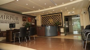 A hotel reception area with a reception desk, chairs, a large decorative wall, and an elevator. - Mirpur Apartments & Hotel (Mirpur)