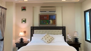 A bedroom with a large bed, a ceiling fan, a window, and a wall-mounted air conditioner. - Mirpur Apartments & Hotel (Mirpur)