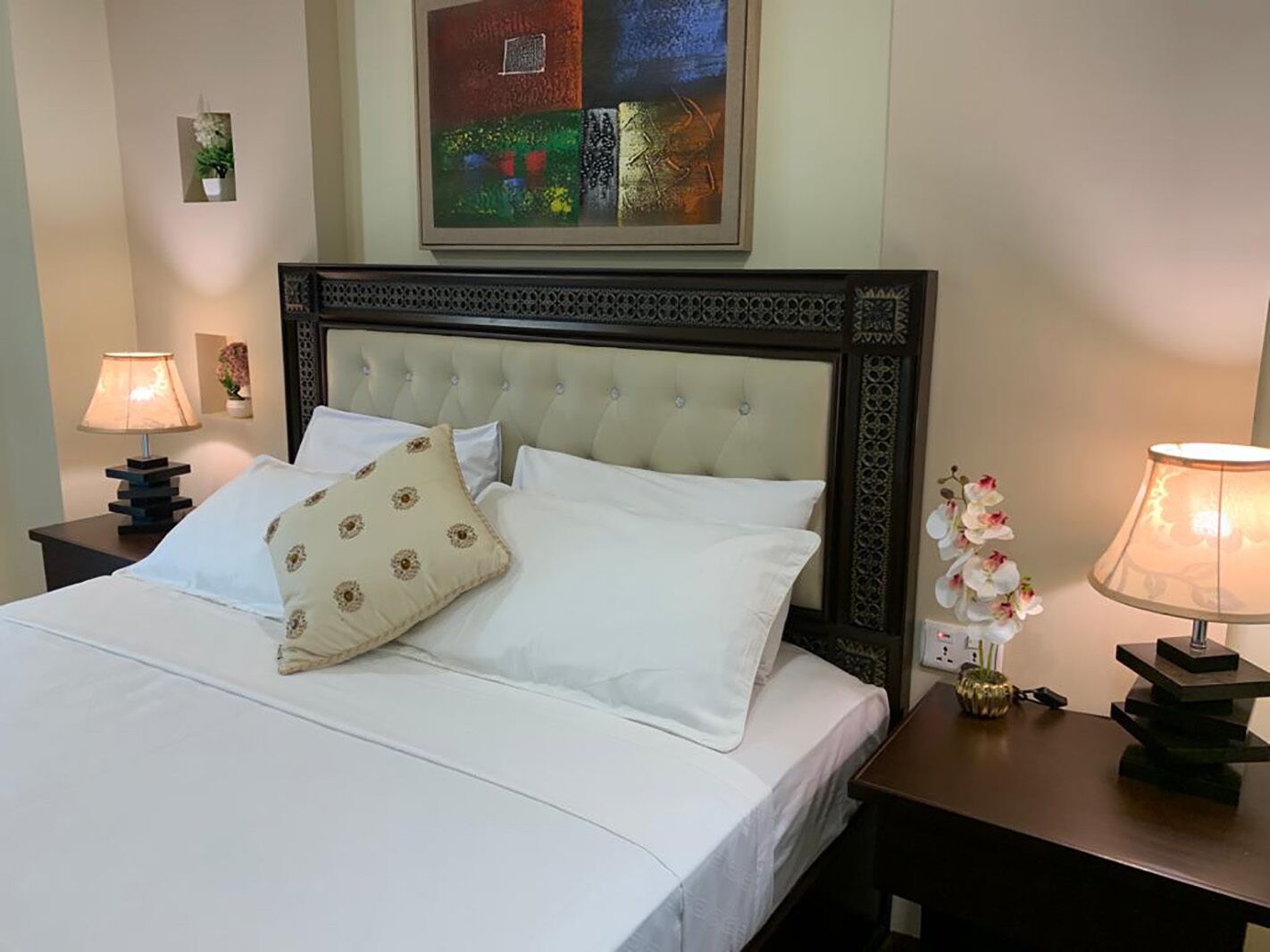 A neatly made bed with white linens and a decorative pillow, flanked by two bedside tables with lamps.