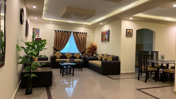 A modern living room with a sectional sofa, a coffee table, and a dining area with a table and chairs. - Mirpur Apartments & Hotel (Mirpur)
