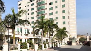 A multi-story hotel with a central courtyard, palm trees, and a clear sky. - Mirpur Apartments & Hotel (Mirpur)