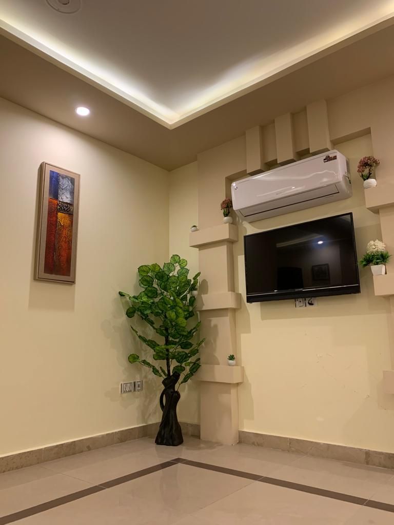 Una sala de estar moderna con un televisor de pantalla plana montado en la pared, una planta grande en maceta y un equipo de aire acondicionado.