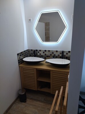 Une salle de bain avec deux lavabos, un miroir hexagonal doté d’un éclairage à DEL et un mur recouvert de carreaux.