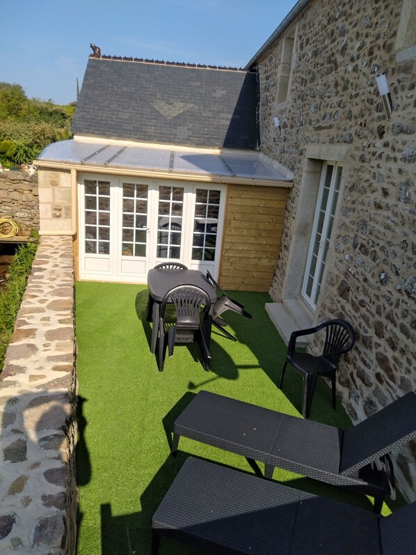 Un espace patio agrémenté d’un mur en pierre, un bâtiment en bois avec un toit en tuiles et une petite table entourée de chaises.