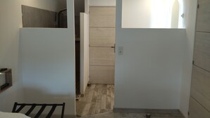 Un pasillo estrecho con una cama a la izquierda, una puerta al final y una pequeña área de cocina con armarios y mostrador.