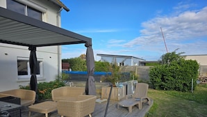 Un patio extérieur couvert, aménagé avec des meubles en osier, une piscine et une terrasse en bois.