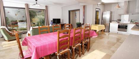 A dining area with a table set for six, wooden chairs, a television, and a kitchen area with a refrigerator and oven.