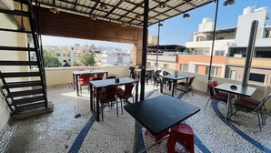 Un área de estar al aire libre con mesas y sillas, piso de baldosas y vista de la ciudad.