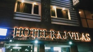Un hotel llamado "HOTEL RAJ VILAS" con letreros iluminados y varias ventanas.