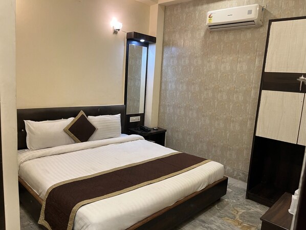 Una habitación de hotel con cama, mesita de noche, espejo y aire acondicionado.