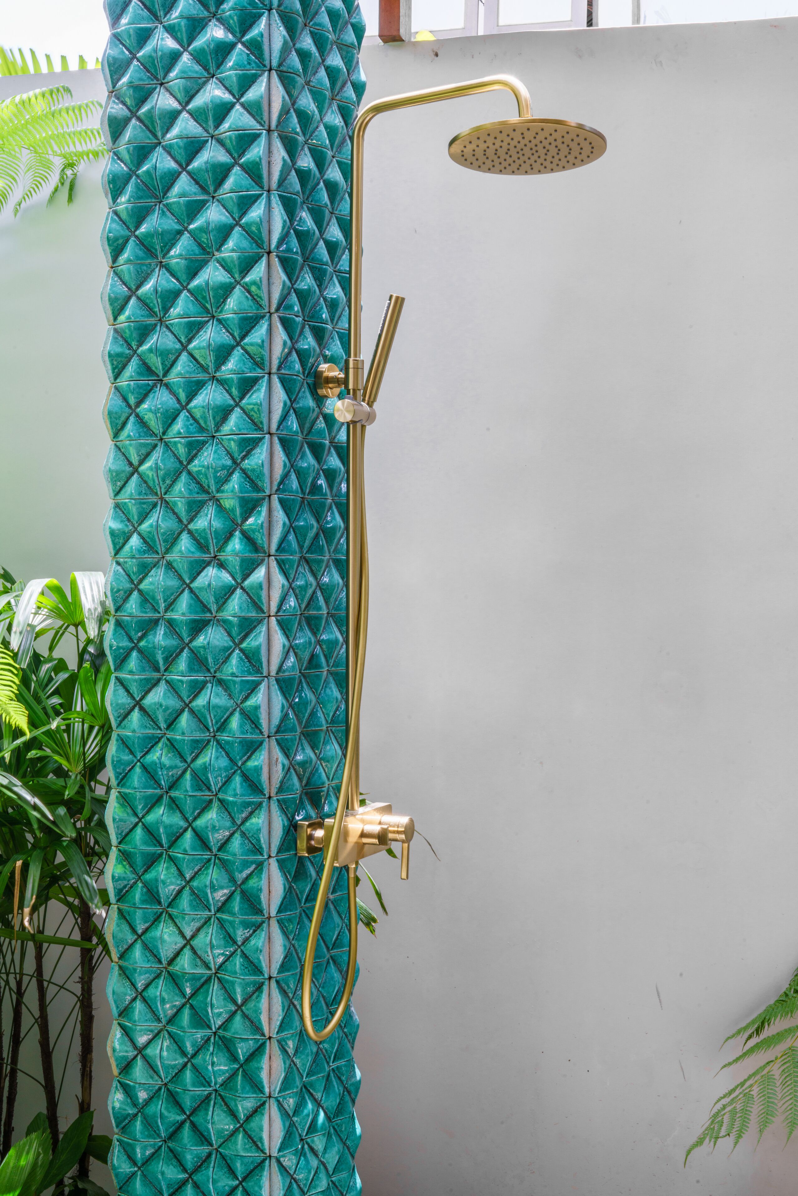 A shower with a gold handle and a round showerhead mounted on a teal textured wall.