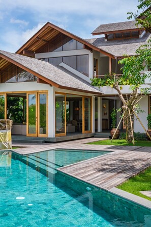 Uma casa moderna de dois andares com piscina, grandes portas de vidro e deck de madeira.