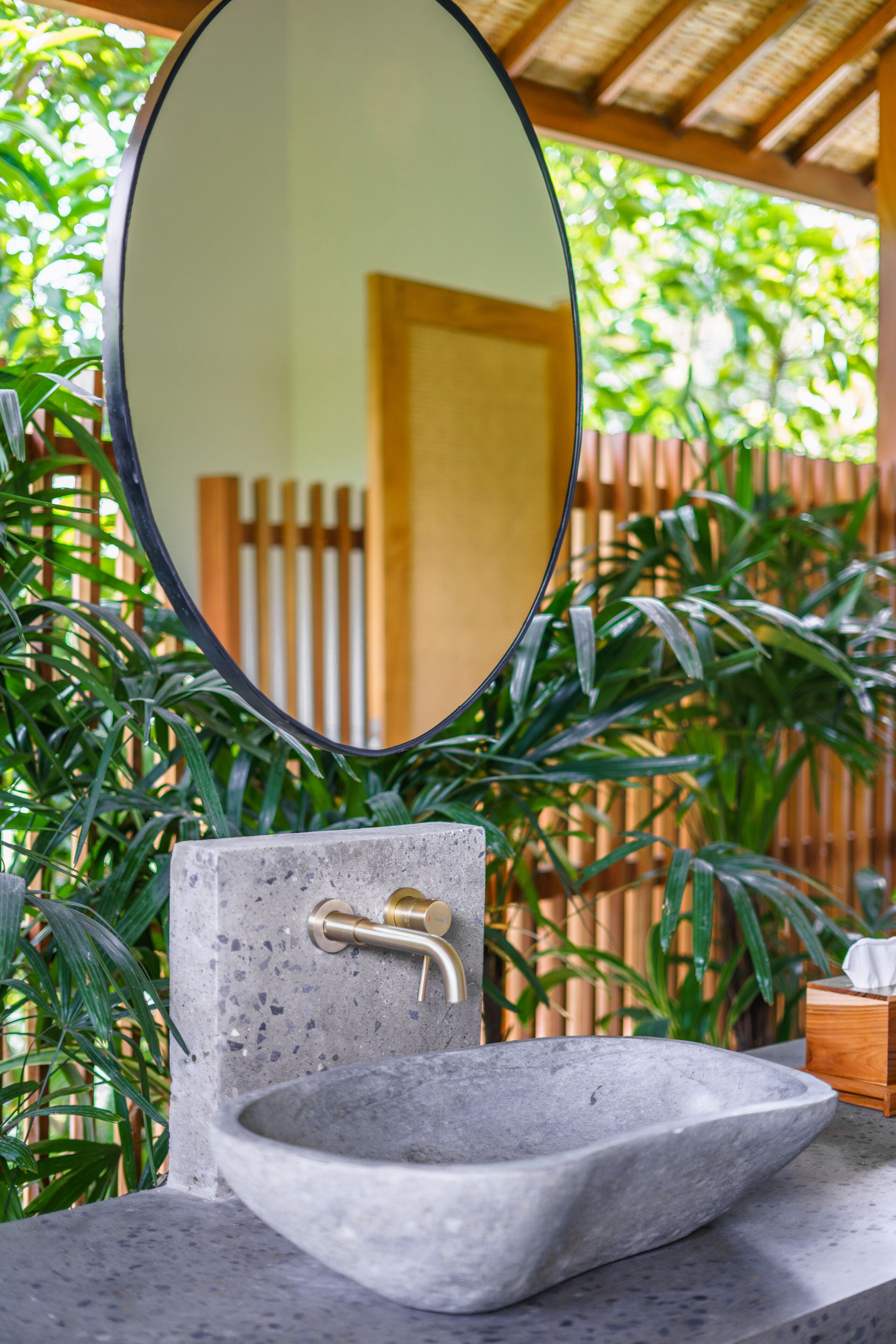 A bathroom with a stone sink, a round mirror, and a wooden door in the background.