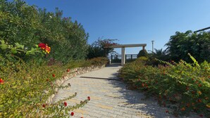 A paved pathway with a pergola structure in the distance, surrounded by lush greenery and flowering plants. - THERETRA KIOTARI VILLAS (Rhodes)