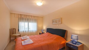 A hotel room with a large bed, a chair, a bedside table with a lamp, and a window with curtains. - THERETRA KIOTARI VILLAS (Rhodes)
