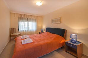 A hotel room with a large bed, a chair, a bedside table with a lamp, and a window with curtains. - THERETRA KIOTARI VILLAS (Rhodes)