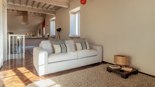 A spacious living area with a white sofa, a wooden coffee table, and a large window providing natural light. - Guest House Bianca (Lucca)