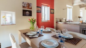 A dining area with a table set for four, a vase with flowers, and a kitchen in the background. - Guest House Bianca (Lucca)