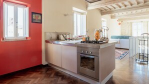 A modern kitchen with a central island, wooden herringbone flooring, and a red accent wall. - Guest House Bianca (Lucca)