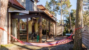 A covered patio with a hammock, glass doors, and a view of the backyard. - Apartment with Garden close to the Beach | Private Parking (Pobierowo)