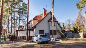 A two-story house with a red-tiled roof, a parked car, and a fenced yard. - Apartment with Garden close to the Beach | Private Parking (Pobierowo)
