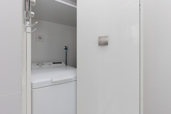 A modern, white laundry room with a built-in washer and dryer, a wall-mounted faucet, and a power outlet.