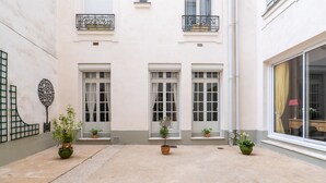 A courtyard with three potted plants, a white building with a balcony, and a window with a curtain. - Postcards from the Eiffel Tower, by Veeve (Paris)